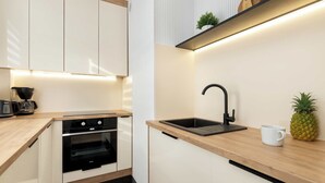 A modern kitchen with white cabinets, a wooden countertop, a black sink, and a coffee maker. - Cozy Apartment with Bedroom | Close to Park and Beach (Gdańsk)