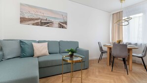 A modern living room with a sofa, a small round table with a plant, and a dining area with chairs and a table. - Cozy Apartment with Bedroom | Close to Park and Beach (Gdańsk)