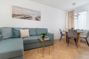 Ein modernes Wohnzimmer mit einer Couch, einem kleinen runden Tisch mit einer Pflanze sowie einem Essbereich mit Stühlen und einem Tisch.