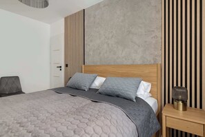 A modern bedroom with a large bed, a bedside table, and a wall with vertical wooden slats.