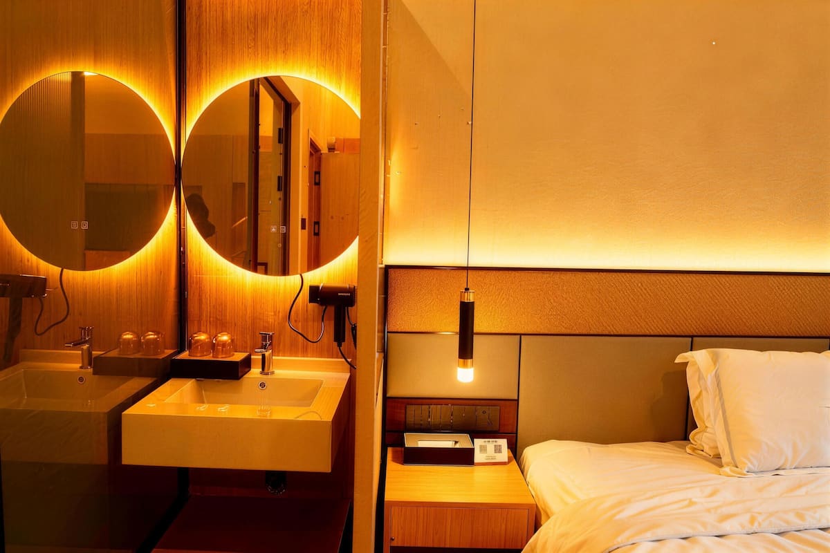 Une chambre d’hôtel avec une coiffeuse en bois, deux miroirs ronds, une table de chevet avec une lampe et un lit avec une literie blanche.