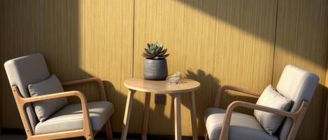 Two wooden chairs with cushions, a small round table with a potted plant, and framed artwork on the wall.