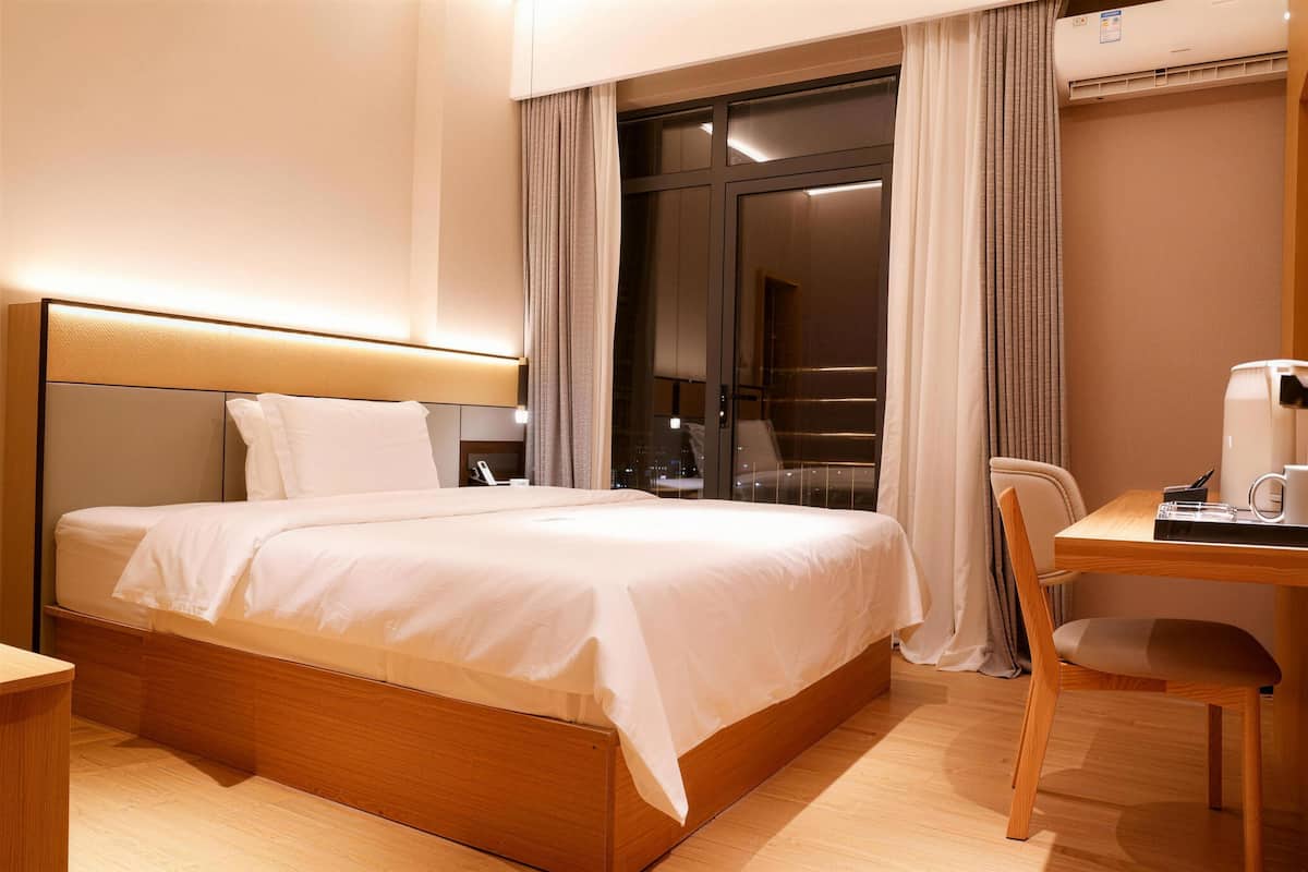 Une chambre d’hôtel avec un grand lit, un bureau avec une chaise et une vue sur la ville par une grande fenêtre.