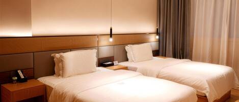 A hotel room with two beds, wooden headboards, a nightstand with a lamp, and a curtain on the window.