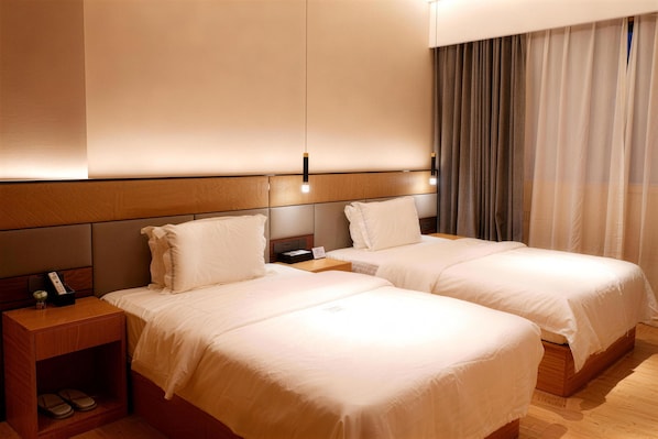 A hotel room with two beds, wooden headboards, a nightstand with a lamp, and a curtain on the window. - 东方翡翠酒店 Jade Hotel (Dar es Salaam)