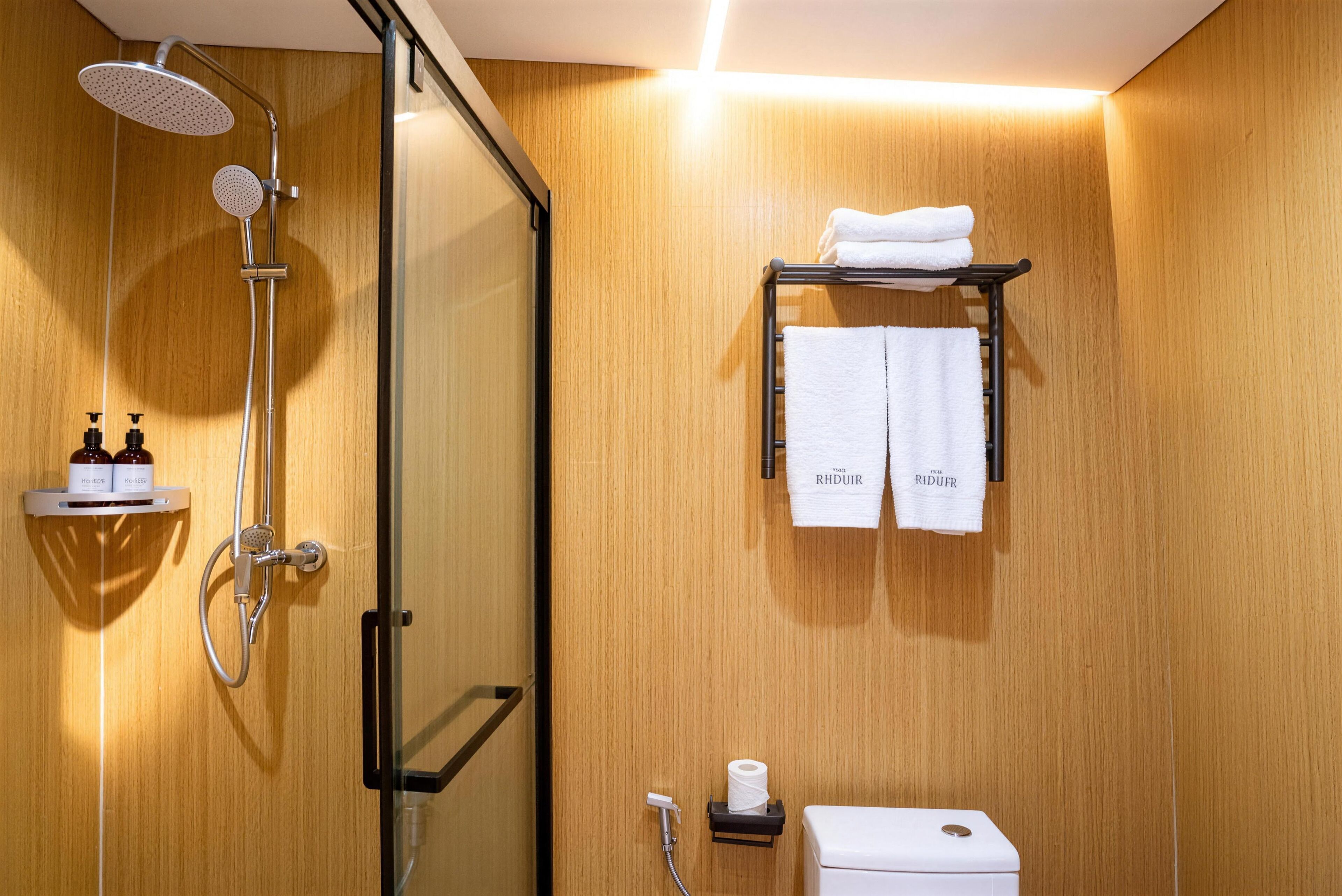 A modern bathroom with a glass shower enclosure, a toilet, and a towel rack with two towels.