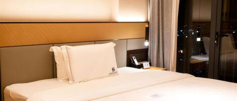 Habitación de hotel con una cama grande, una mesita de noche con teléfono y vistas a la ciudad a través de la ventana.