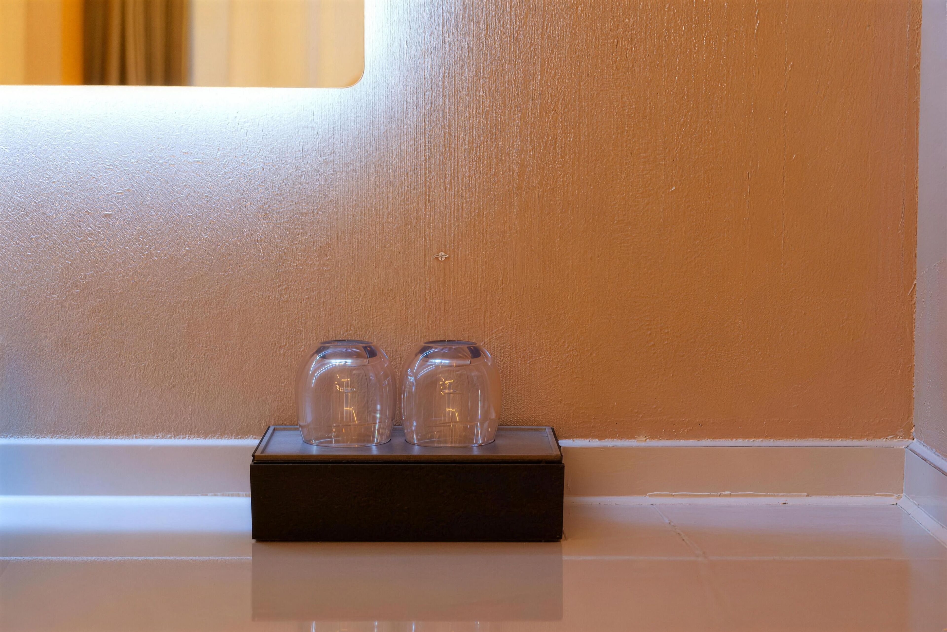 A black tray with two clear glass jars on a white surface against a beige wall.