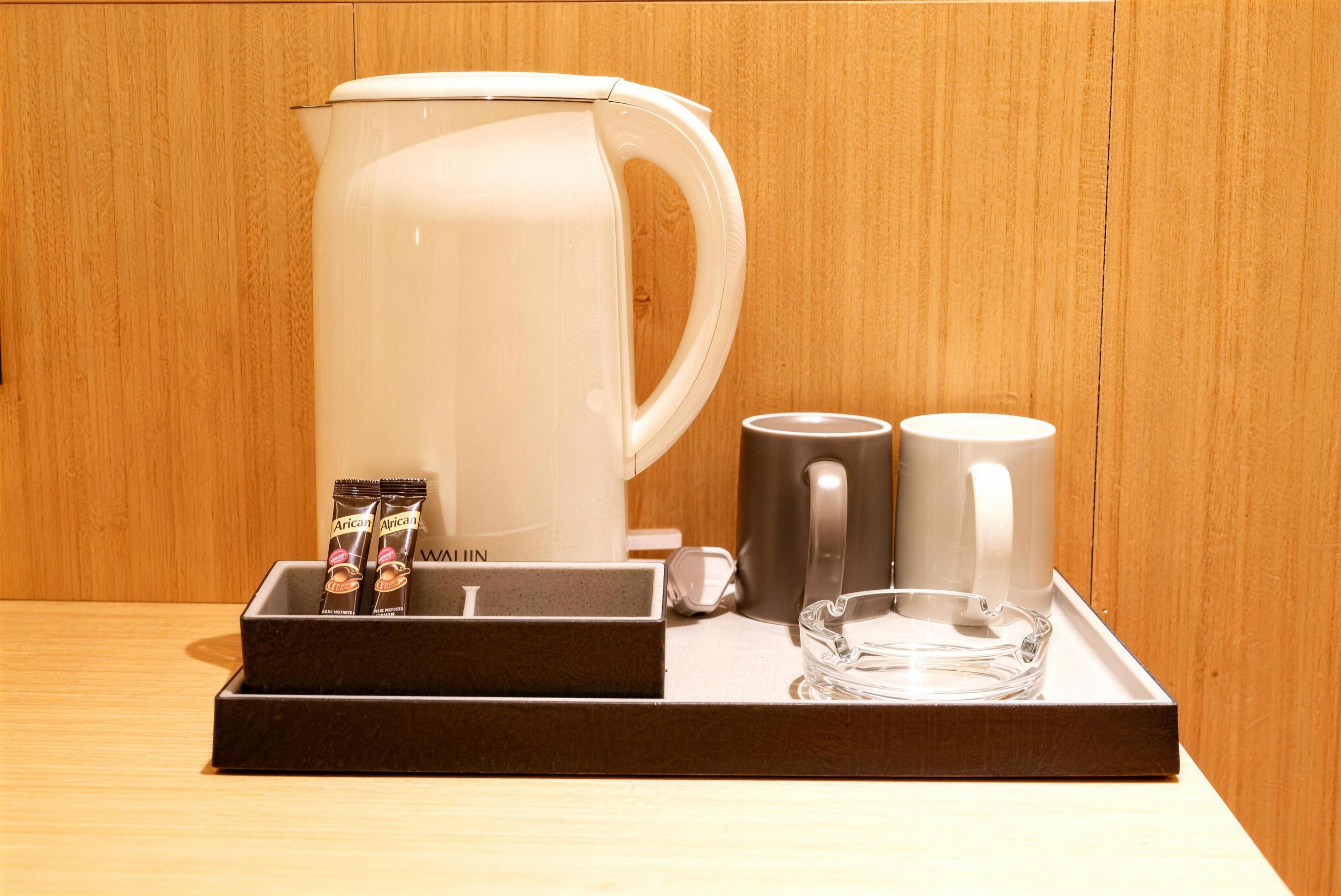 A coffee station with a white coffee maker, two mugs, a glass, and two packets of coffee.