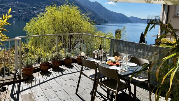 Eine Terrasse mit Tisch für zwei Personen, mit Blick auf einen See und Berge.