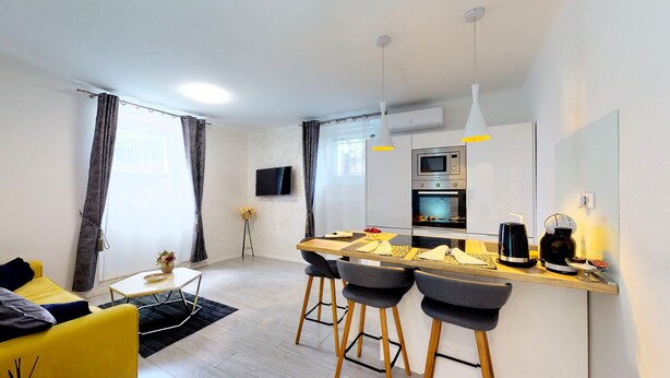 A modern kitchen with a central island, bar stools, a flat-screen TV, and an oven. - Apartment Nila by Litto (Split)