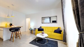 A modern living space with a yellow sofa, a small white table, and a kitchen area with a bar stool. - Apartment Nila by Litto (Split)