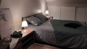 Ein Schlafzimmer mit einem Bett, zwei Nachttischen, einer Lampe, einem Wandregal und einem Fenster.