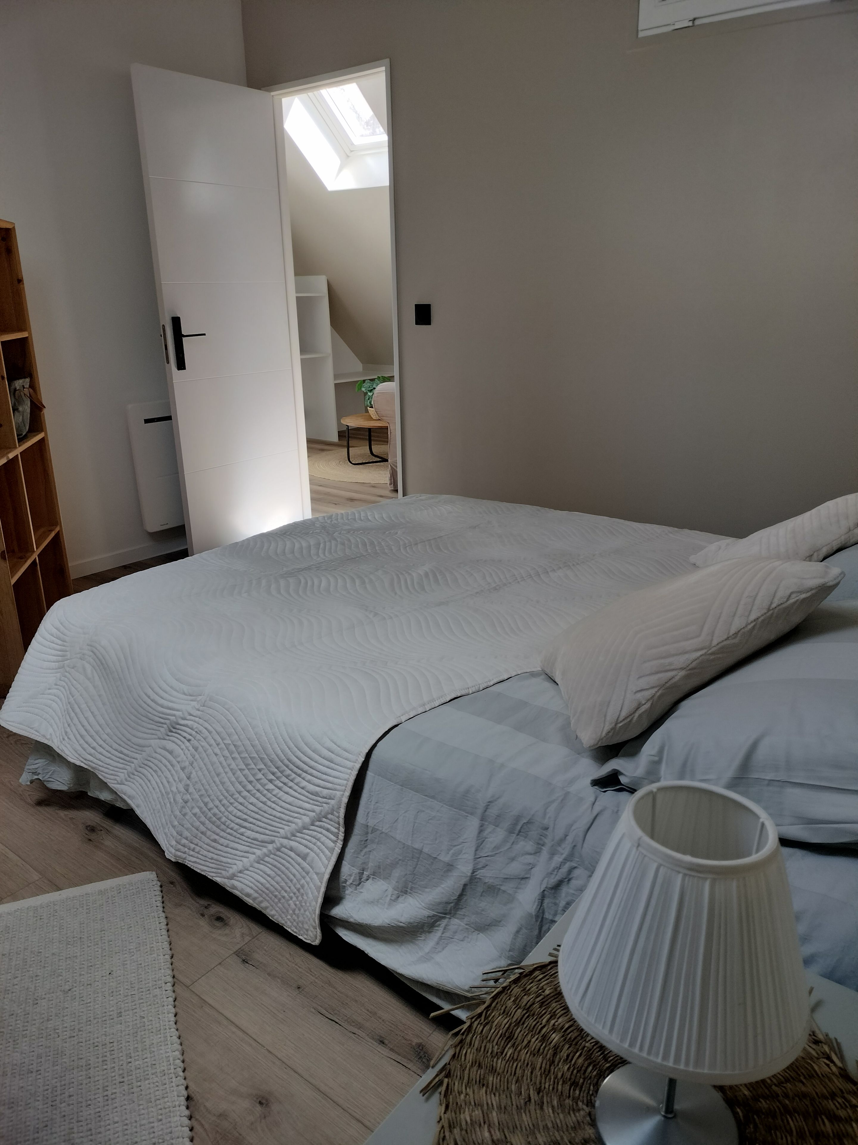 Een slaapkamer met een groot bed, een bedlampje, een houten vloer en uitzicht op een trap naar een verdieping erboven.