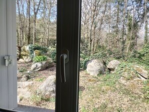A view through a door into a forested area with large rocks and greenery.