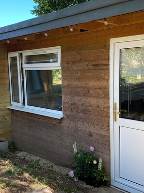A wooden cabin with a white door and window, surrounded by a garden with flowers and plants.