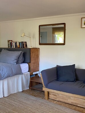 A bedroom with a bed, a wooden nightstand, a bedside table with a lamp, a bookshelf, a mirror, and a sofa.