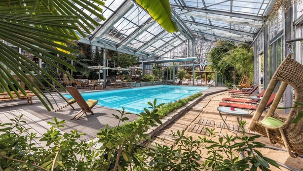 An indoor swimming pool with a glass ceiling, surrounded by lounge chairs and potted plants. - New modern apartments for active vacationers with wellness and pool. Dog friendly (Goldrain)