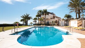 A swimming pool with a curved edge, surrounded by palm trees and a building with balconies. - La Joya Stunning Sea Views by Alfresco Stays (Mijas Costa)