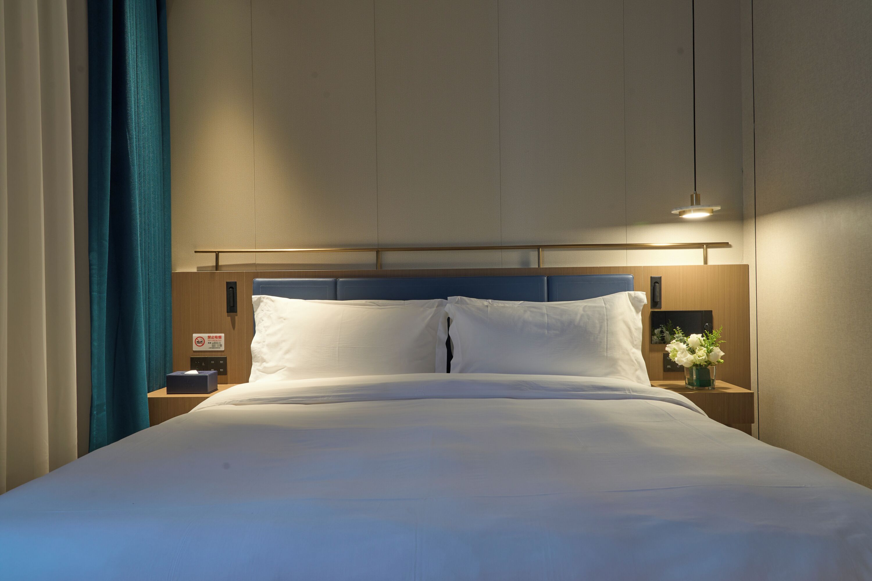 A neatly made bed with white linens, a wooden headboard, a bedside table with a lamp, and a nightstand with a tissue box.
