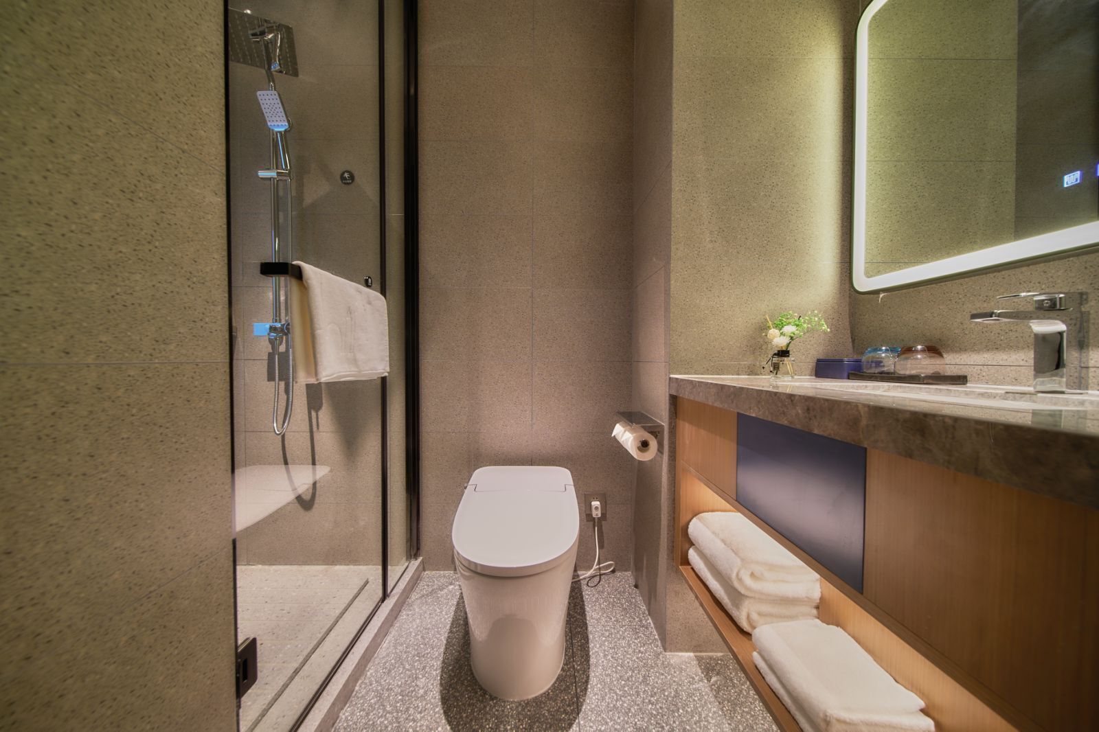 A modern bathroom with a glass shower enclosure, a toilet, a sink with a mirror, and neatly folded towels.