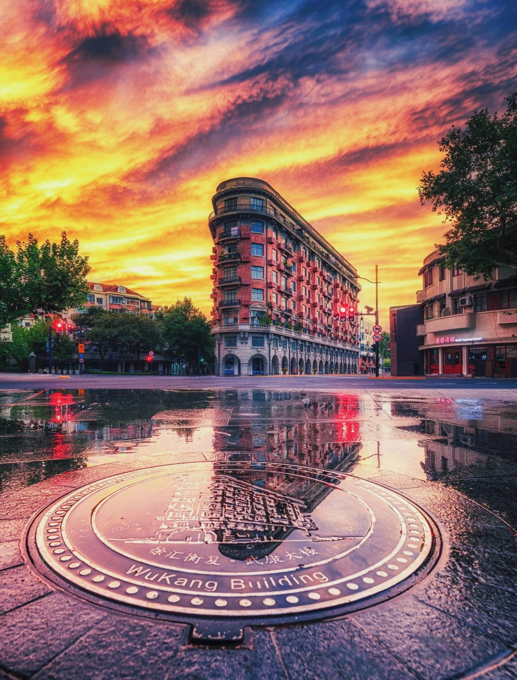 A building with a curved facade, a manhole cover with text, and a reflection in a puddle.