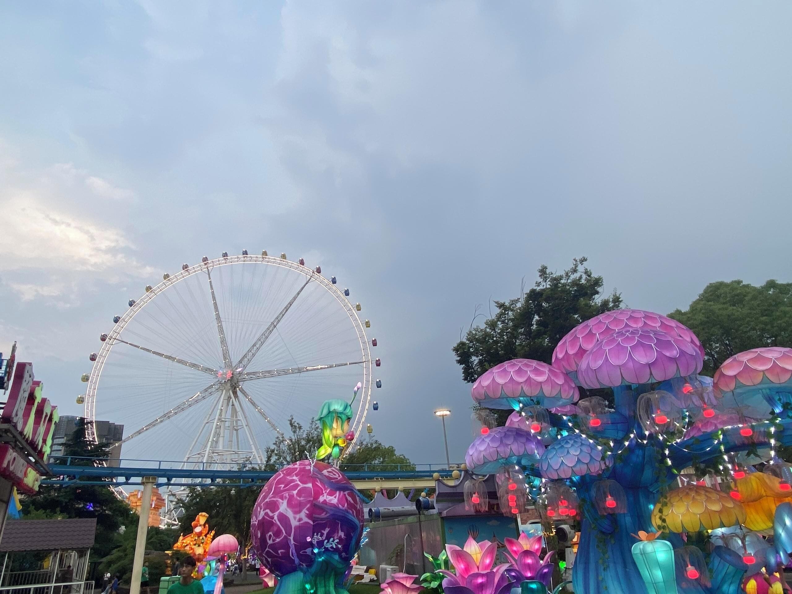 Une grande roue et des structures colorées en forme de champignons dans un parc d’attractions.