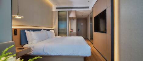 Une chambre d’hôtel moderne avec un grand lit, une table de chevet et un téléviseur fixé au mur.