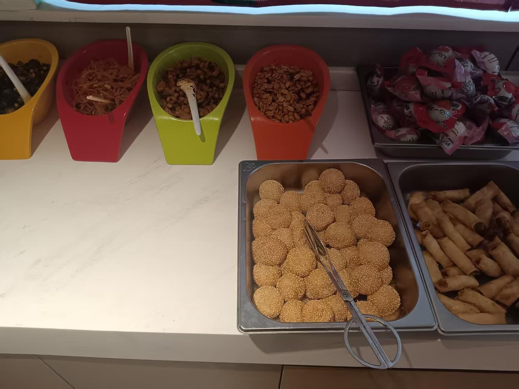 Un buffet proposant une variété de plats présentés dans des bols et des plateaux colorés, notamment des boules de sésame et des rouleaux de printemps.