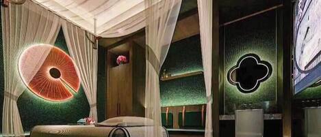 A room with a bed, a small table, a chair, a decorative wall, and a large window.