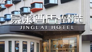 Een hotelentree met een modern ontwerp, met grote glazen deuren en een bord met de naam 'JINGLAI HOTEL'.