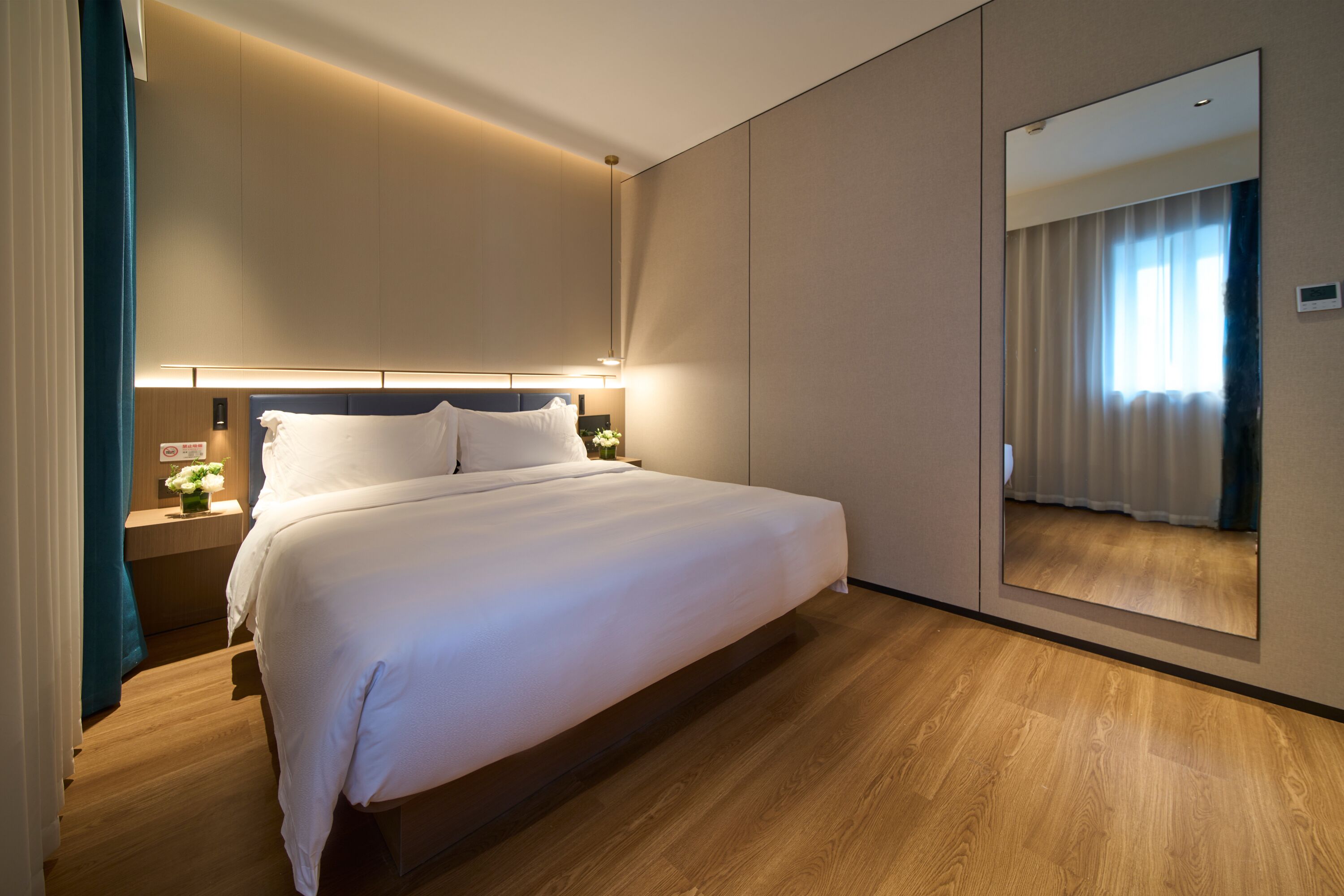 A modern hotel room with a large bed, bedside tables, a mirror, and a wooden floor.
