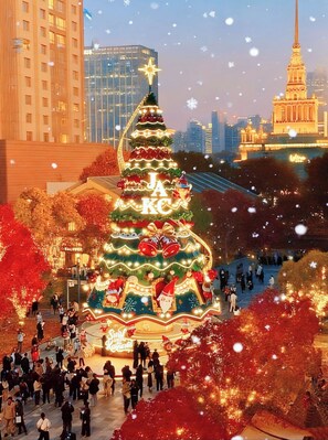 Ein großer, beleuchteter Weihnachtsbaum mit dem Schriftzug 'JAKE', umgeben von Menschen in einer städtischen Umgebung mit Gebäuden im Hintergrund.