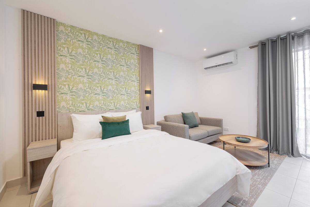 A modern hotel room with a large bed, a sofa, a small coffee table, and a patterned wall.