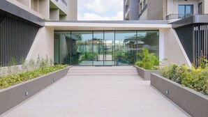 Une entrée moderne avec des portes en verre, une rampe d’accès et de la verdure environnante.