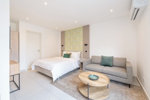 A modern bedroom with a bed, a sofa, a coffee table, and a decorative wall panel. - The Bantree (Accra)