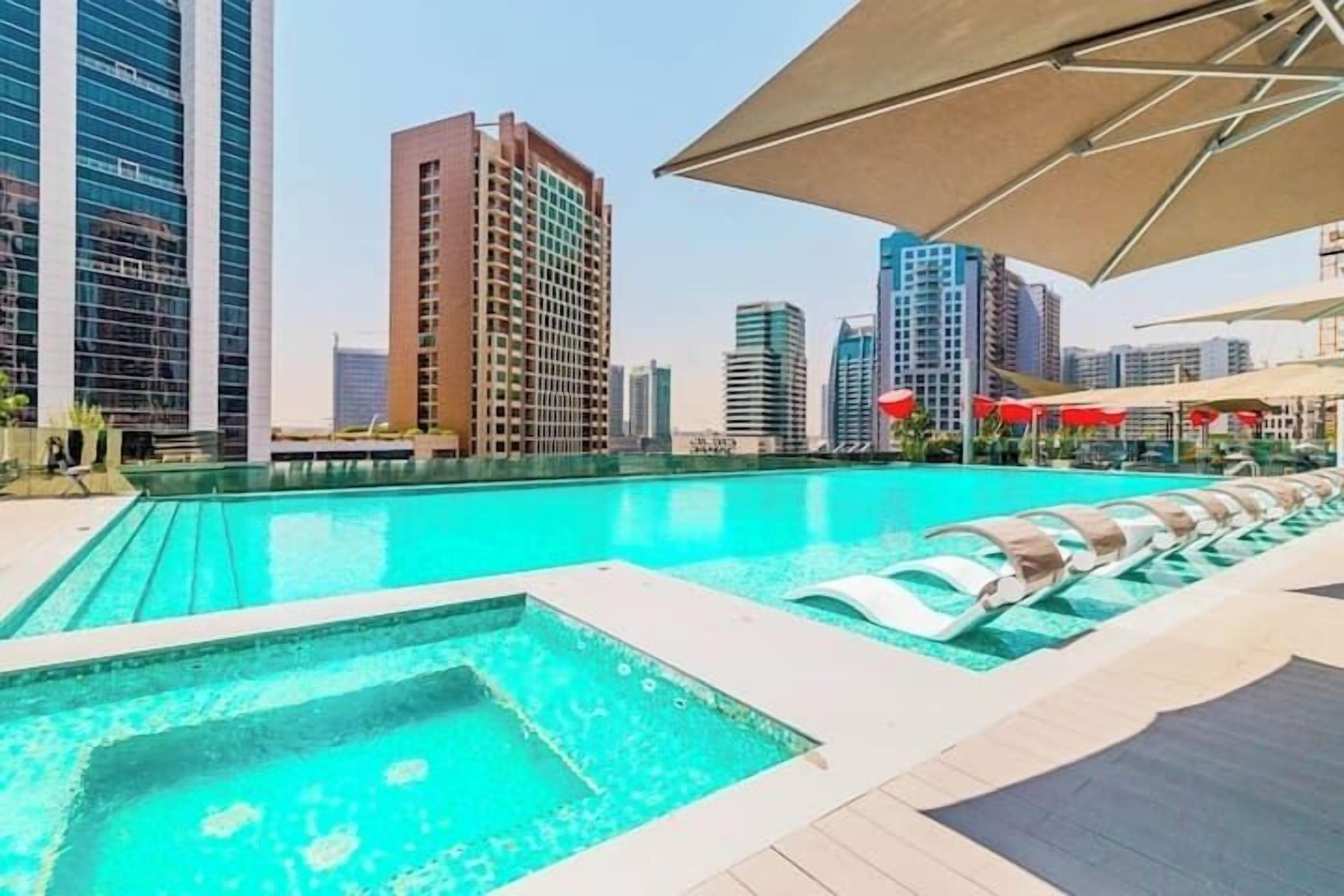 A swimming pool with lounge chairs and umbrellas, surrounded by high-rise buildings.