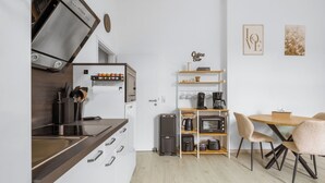 Eine kompakte Küche mit Backofen, Kaffeemaschine und kleinem Kühlschrank. Es gibt eine Essecke mit einem Holztisch und Stühlen.