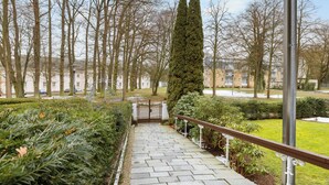 Ein gepflasterter Weg führt zu einem ehrwürdigen Eingangstor, umrahmt von geschnittenen Hecken und hohen Bäumen.