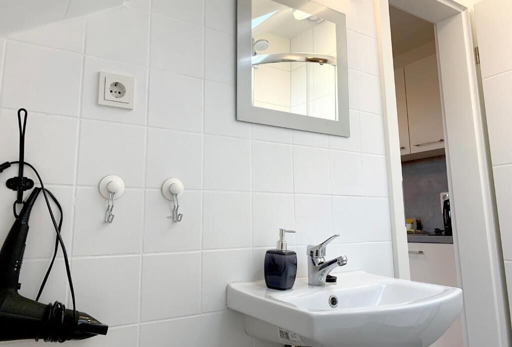 Ein Badezimmer mit einem weißen Waschbecken, einem Spiegel und einem Haartrockner auf einem Ständer.
