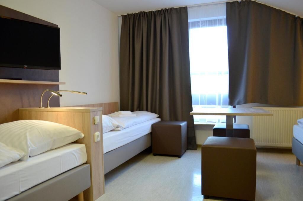 Habitación de hotel con cama, escritorio, silla, televisor y cortinas.