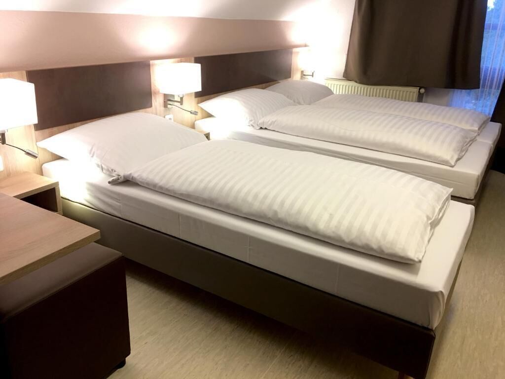 Habitación de hotel con dos camas, cada una con ropa blanca y cabeceros. Hay lámparas de noche y mesitas de noche con lámparas.