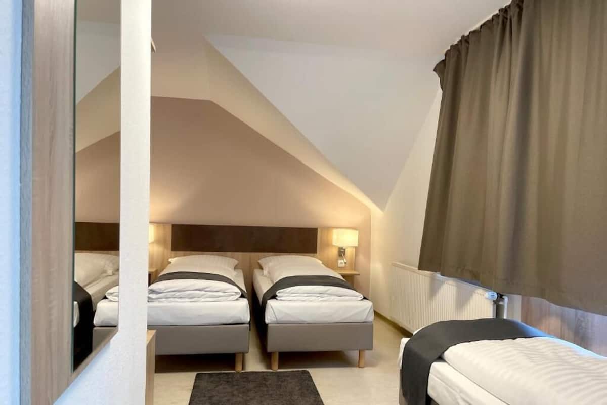 Una camera d'albergo con due letti, un grande specchio, un tappeto scuro e una finestra con tende.