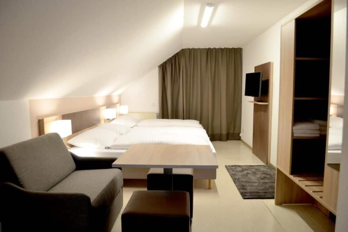 Una camera d'albergo con un letto, un divano, un tavolo, una TV e un armadio.