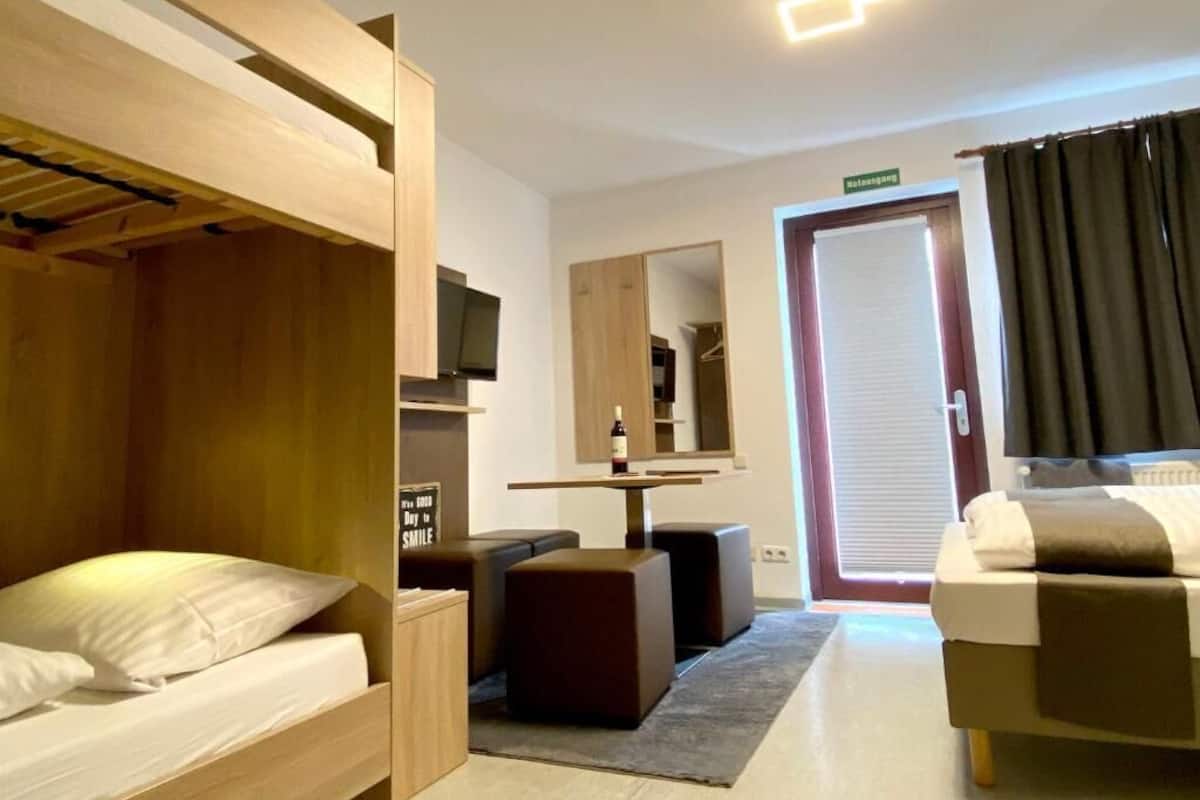 Camera d'albergo moderna con un letto a castello, un divano, un tavolino con una bottiglia, uno specchio e una porta con tende.