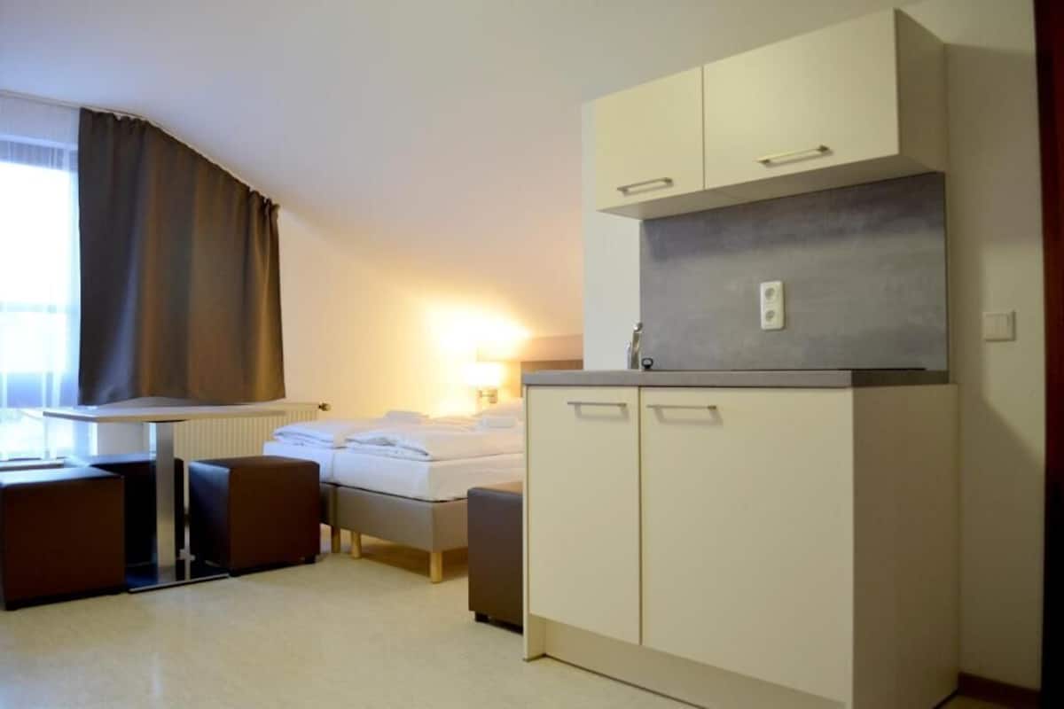 Una camera d'albergo compatta con un letto, un angolo cottura, una scrivania e una finestra con tende.