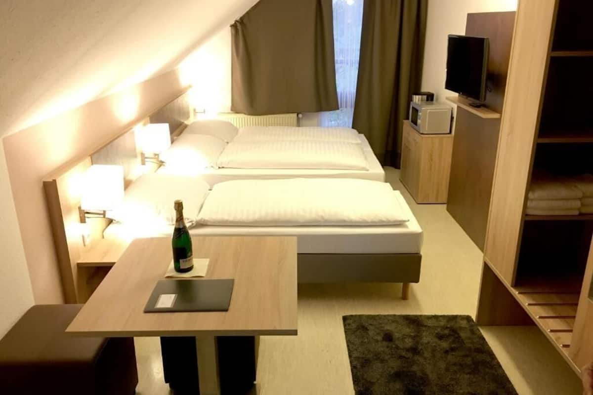 Una camera d'albergo con un letto, comodini, una televisione e una piccola scrivania con una bottiglia.