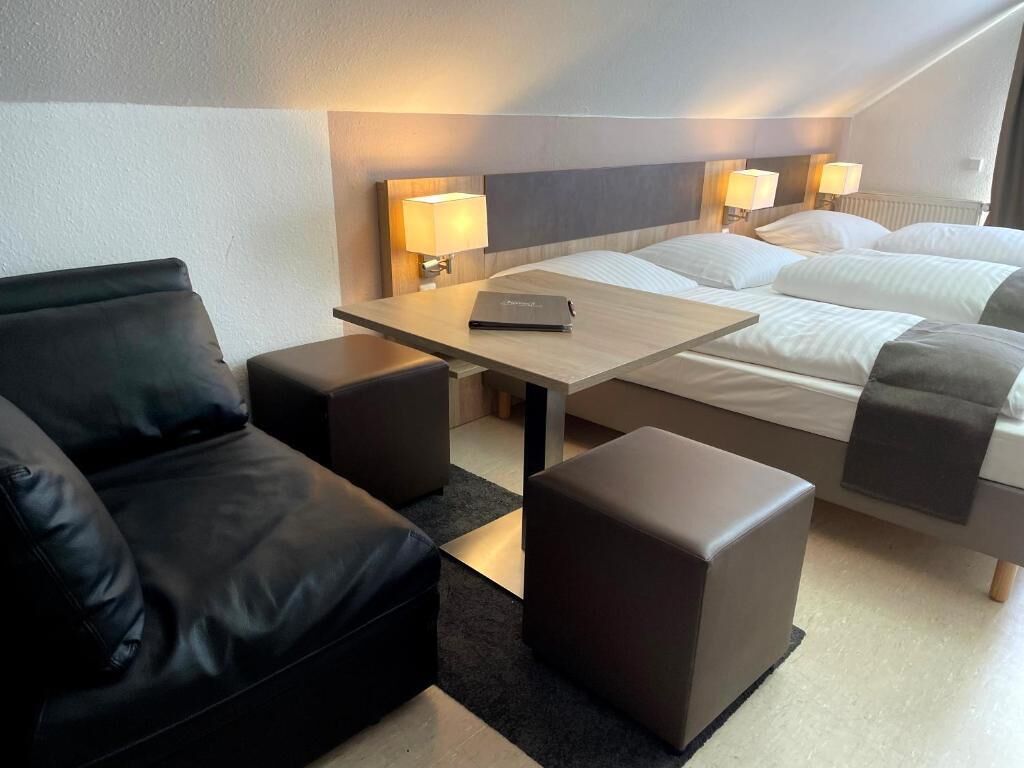 Una habitación de hotel con cama, escritorio, silla y un pequeño reposapiés.