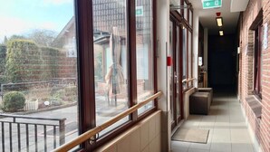 A corridor with large windows, a fire exit sign, and a tiled floor. - Hana Aparthotel (Barsbuttel)