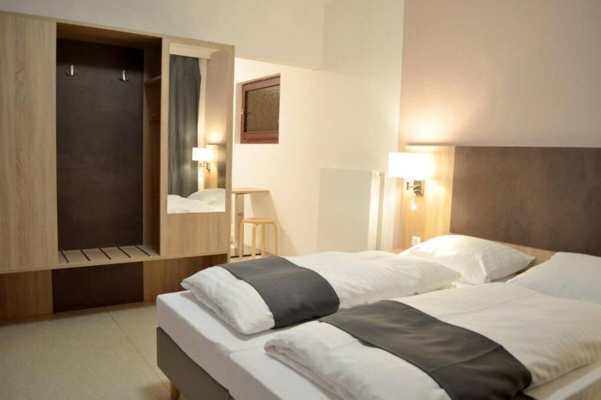 Una camera d'albergo con due letti, un guardaroba in legno, un tavolino e lampade a parete.